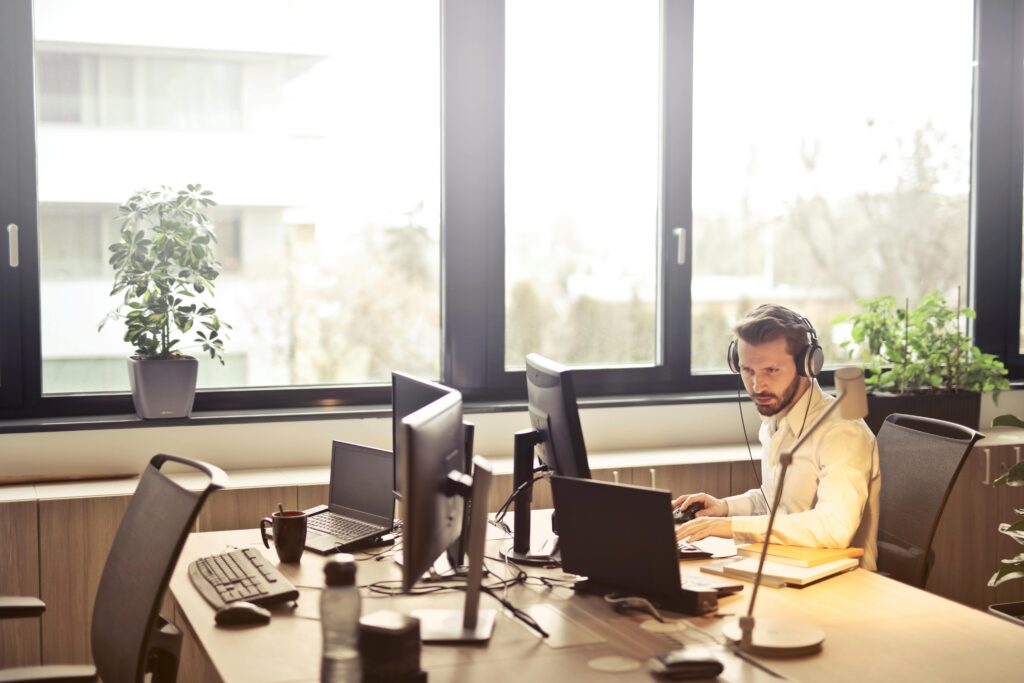 pexels-photo-845451-845451 A businessman sits at a desk using multiple computers and a headset in a well-lit modern office.